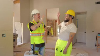 İki hevesli inşaat işçisi zorlu bir yenileme projesinde kaydettikleri olağanüstü ilerlemeyi coşkuyla kutluyorlar. Birbirlerine tezahürat yaparak ve gülümseyerek, canlı bir şekilde gerçek takım çalışması sergileyerek.