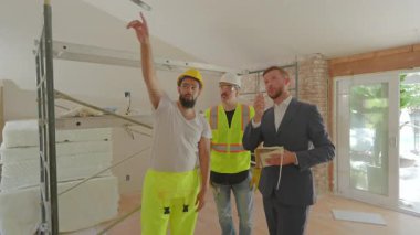 Üç deneyimli inşaat işçisi, devam eden yenileme çalışmalarını değerlendirmek ve işbirlikçi proje planlama ve uygulamaya olan bağlılıklarını göstermek için açık bir alanda toplandılar.