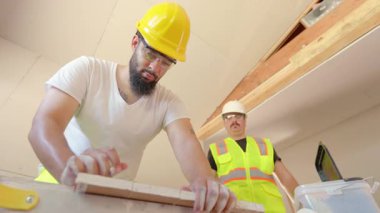 Parlak ışıklandırılmış bir atölyede, iki çok yetenekli profesyonel, ahşap tahtaları büyük bir doğrulukla ölçmeye ve işaretlemeye yoğunlaşarak, işlerinde en yüksek kalitede işçiliği sağlıyorlar.