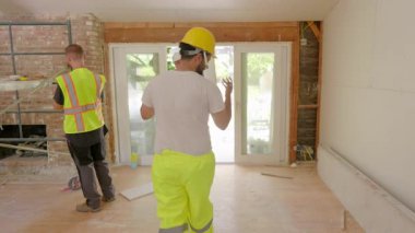 Çalışan bir inşaat sahasında ev yenileme çalışmaları yapan yetenekli bir ekip, takım çalışmasının ve projelerinde verimlilik ve kalite planlamasının önemini vurguluyor.