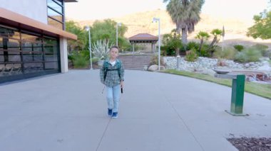 Neşeli bir çocuk, çeşitli renkli çiçeklerle dolu canlı ve gür bir alanda mutlu bir şekilde dolaşırken, aynı zamanda manzarayı güzelleştiren modern bir binanın yanında.