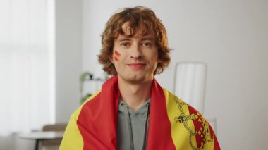 Gülümseyen İspanyol futbol taraftarı favori İspanya takımı için tezahürat yapıyor, yanaklarında boyalı bayraklarla. Avrupa Spor Futbol Kupası. Dünya 2026 ABD, Kanada, Meksika. Futbol, spor ve futbol fanatikleri. Yavaş Hareket