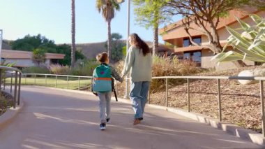 Sevgi dolu bir anne ve neşeli çocuğu, verimli yeşillik ve modern mimari ile çevrili güneşli bir patika boyunca el ele gezintiye çıkarlar.