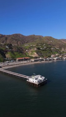 Hava görüntülerinde Malibu Rıhtımı, canlı okyanus dalgaları ve yemyeşil tepeler, Kaliforniya 'nın çarpıcı sahil şeridini mükemmel bir şekilde aydınlatıyor ve dinleyicileri dingin cazibesini takdir etmeleri için davet ediyor.