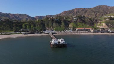Hava görüntülerinde Malibu Rıhtımı, canlı okyanus dalgaları ve yemyeşil tepeler, Kaliforniya 'nın çarpıcı sahil şeridini mükemmel bir şekilde aydınlatıyor ve dinleyicileri dingin cazibesini takdir etmeleri için davet ediyor.