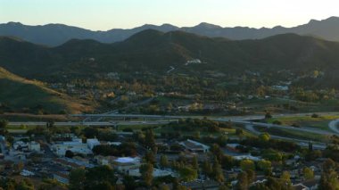 Los Angeles 'ın banliyösünü gösteren hava görüntülerinde muhteşem yeşil tepeler, muhteşem dağlar ve çarpıcı bir gün batımı sırasında hareketli çevre yolu trafiği görülüyor.