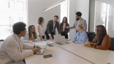 Canlı bir konferans odasında, yetenekli iş adamlarından oluşan çeşitli bir ekip finansal verileri ve ayrıntılı satış raporlarını inceleyerek çabalarını artırmak için dizüstü bilgisayarlarını kullanarak işbirliği yapıyor.