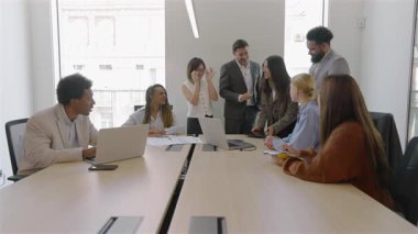 Modern bir konferans odasında, çeşitli iş adamları işbirliği yapar, finansal verileri analiz eder ve satış raporlarını tartışır, patronlarını alkışlar, kurumsal büyüme ve başarı kararları