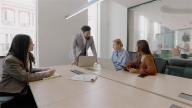 Modern bir ofiste, gerek erkek gerekse kadın profesyonellerden oluşan çeşitli bir grup, dizüstü bilgisayarlarla yapılan verimli bir toplantıda, ortak hedefler ve yenilikler doğrultusunda takım çalışması sergilemektedir.