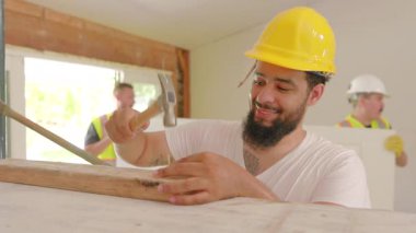 Aralarında Afro-Amerikan, İspanyol ve Kafkasyalı işçilerin de yer aldığı çeşitli inşaatçılar, bir ev yenileme, sergilenen takım çalışması ve işçiliği için yoğun bir inşaat sahasında işbirliği yapıyorlar.