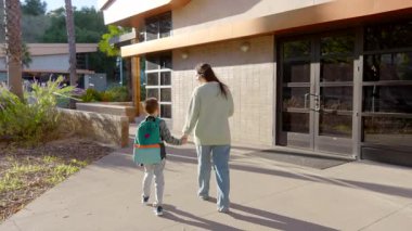 Dokunaklı ve iç açıcı bir sahne, sevgi ve şefkat dolu, aydınlık bir günde, modern bir binaya doğru el ele yürüyen sevgi dolu bir anne ve küçük çocuğunu tasvir eder.