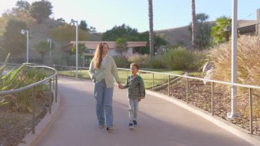 Güneşli bir günde, sevgi dolu bir anne çocuğuyla canlı bir parkta el ele yürür, değerli anların tadını çıkarır ve doğanın neşeli görüntüsü ve sesleri arasında kalıcı anılar yaratır.