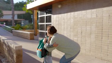 Güzel, güneşli bir sabah ebeveyni, oğlunu okula göndermeden önce sıcak bir şekilde kucaklıyor derin bir sevgi ve içtenlikle dolu çok önemli bir anı yakalıyor.