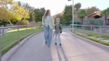 Sevgi dolu bir anne ve küçük çocuğu, bereketli ve canlı yeşilliklerle çevrili sakin ve huzurlu bir park yolu boyunca neşeyle el ele yürür ve büyüleyici günbatımının sıcacık parıltısıyla aydınlanır.