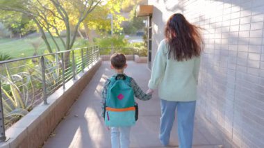 Canlı ve renkli bir sırt çantasıyla süslenmiş genç bir çocuk neşeli bir yetişkinin yanında mutlu bir şekilde yürüyor. İkisi de güneşli bir günün tadını çıkarıyorlar.