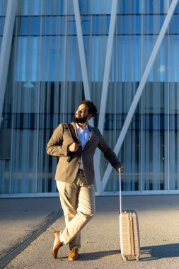 İyi giyimli bir adam, modern ve çağdaş bir binanın önünde durmuş, bavulunu tutarken, şık, gezgin bir görünüm sergiliyor, oldukça iyi bir izlenim bırakıyor.