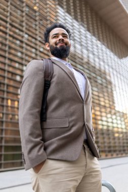 İyi giyimli bir işadamı, çağdaş, şık, modern bir binanın önünde duruyor. Görkemli bir duruşuyla profesyonelliğini, zarafetini ve şık duruşunu gözler önüne seriyor.