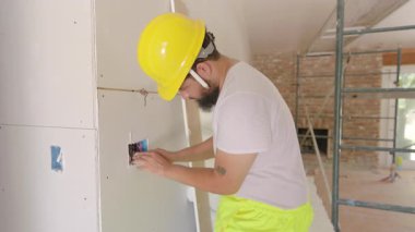 Sarı kask takan Afrikalı Amerikalı işçiler, inşaat sahasında duvara elektrik bağlıyorlar, ellerini ve aletlerini yenileme ve gelecek planlama için kullanıyorlar.