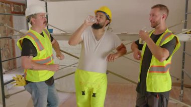 Aralarında İspanyol, Afro-Amerikan ve Kafkasyalı şahısların da yer aldığı çeşitli inşaatçılar, yoğun bir inşaat sahasında işbirliği yaparak, yeni bir ev yenileme projesinin planlarını tartışıyor.