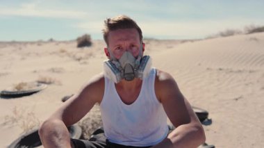 Issız bir çölde, solunum maskeli bir adam, kötü koşullarda izolasyon, dayanıklılık ve hayatta kalma temalarını vurgulayarak, kıyamet gibi bir toprak ve enkaz atmosferi taşır.