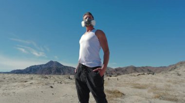 Solunum cihazı ve kolsuz bluz giyen bir adam zorlu zorluklara karşı kararlılığı simgeler, acımasız çöl manzarasında şiddetli bir izolasyon içinde hayatta kalma mücadelesini somutlaştırır.