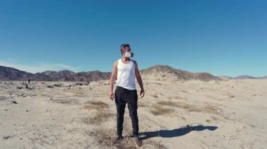 Issız bir çölde, solunum maskesi takmış bir adam posttapokaliptik bir dünya olan kirliliğe ve terk edilmeye karşı hayatta kalmayı simgeler.