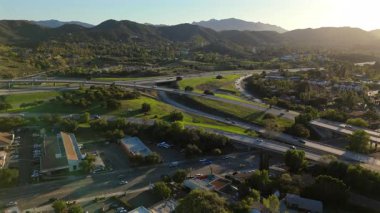 Los Angeles, Kaliforniya 'nın büyüleyici bir banliyösünde bulunan yemyeşil tepelerin arasına yerleşmiş genişleyen bir otoyol kavşağının çarpıcı, etkileyici hava manzarası.