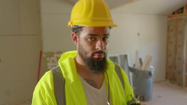 Yoğun bir şantiyede, parlak sarı başlıklı kendini adamış bir inşaat işçisi güvenlik gözlüklerini ayarlıyor ve yenileme çalışmaları sırasında güvenlik protokollerine bağlı kalmanın önemini vurguluyor.