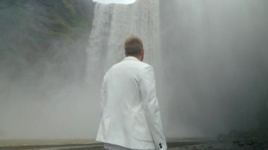 Genç bir adam İzlanda 'daki görkemli Skogafoss şelalesinin karşısında duruyor. Etrafı tamamen dönen sisle çevrili ve doğanın nefes kesici güzelliğiyle çevrili.