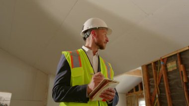 Güvenlik teçhizatı mühendisi, yoğun bir inşaat alanını inceleyip ayrıntılı notlar alıyor. Bu süreç, projelerin inşası için hayati önem taşıyan temel proje yönetim becerilerini vurgular