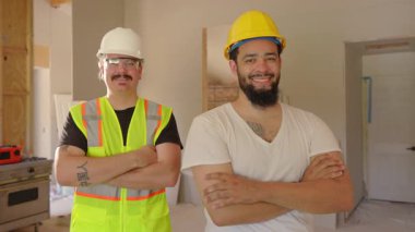 Güvenlik donanımlı iki neşeli inşaat işçisi yenilenmiş bir alanda gururla duruyor, ilerlemeyi ve kendini adamayı sembolize eden bir proje alanında profesyonellik ve takım çalışması sergiliyorlar.