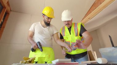 Yoğun bir inşaat alanında, güvenlik yelekleri ve miğferler üzerinde çalışan iki yetenekli işçi, devam eden bir proje için araçlar ve ölçüm materyalleri kullanarak, her şeyin doğru ve kurallara uygun olmasını sağlayarak işbirliği yapıyorlar.