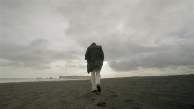 Genç adam, Reynisfjara 'nın kara kumları boyunca sakin ve el değmemiş Güney Sahili' nin nefes kesen güzelliğini içine çekerek rahatça dolaşır.
