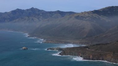 Bu hava manzarası California kıyı şeridini yakalıyor, Big Sur ve ikonik 1. Otoyol 'u gösteriyor. Görkemli dağlar gün batımında dalgalarla karşılaşıp doğal güzellikleri sersemleten alanları vurguluyor.