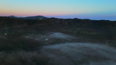 Çarpıcı Malibu dağlarının nefes kesici hava manzarası, yemyeşil tepelerin büyüleyici ve büyüleyici bir günbatımı sırasında güzel bir sis ve bulutla kaplandığı yer.