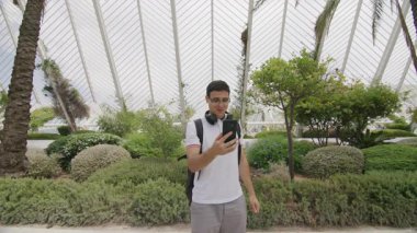 Kulaklıkları ve sırt çantasıyla dışarıda selfie çeken aktif bir genç. Moda, genç blog yazarı egzotik doğal ortamda seyahat ederken videolar yayınlıyor. Yüksek kalite 4k görüntü