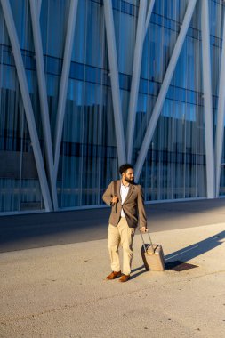 Canlı bir şehirde, kendine güvenen özel takım elbiseli bir adam şık bir evrak çantasıyla parlak bir şekilde yürüyor, başarılı şehir yaşam tarzını ve şehrin dinamik enerjisini yansıtan parlak cam bir binanın önünden geçiyor.