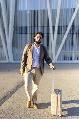 Şık bir bavulu olan kendine güvenen bir işadamı çarpıcı çağdaş mimarinin önünde gururla duruyor, modernliği somutlaştırıyor ve hareketli şehir manzarasında sakin bir tavır sergiliyor.