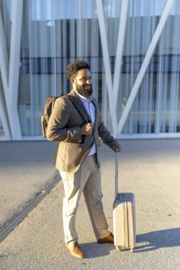 Zarif bir bavulu olan sofistike bir adam çarpıcı ve modern çağdaş bir binanın önünde duruyor. Modern seyahat, keşif ve zarafetinin özünü yansıtıyor.