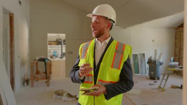 Sıkı bir şapkayla birlikte çelik yelek giyen bir müteahhit inşaat alanını inceliyor. Kaydedilen ilerlemeler ve uygulanan güvenlik önlemleri hakkında özenle not alıyorlar.