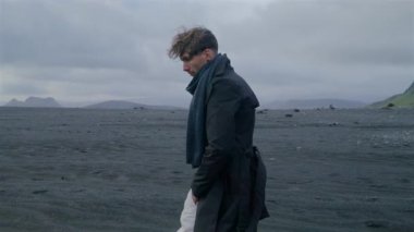Genç adam Reynisfjara sahilinde geziniyor, eşsiz siyah kumların İzlanda 'nın büyüleyici manzaralarıyla buluştuğu yerde, derin bir yansıma ve iç huzur için mükemmel büyüleyici bir atmosfer yaratıyor.