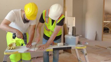 İki inşaat işçisi, devam etmekte olan proje ve görevleri için aletlerini dikkatli bir şekilde kullanarak çeşitli materyalleri ölçüyor ve kesiyor.