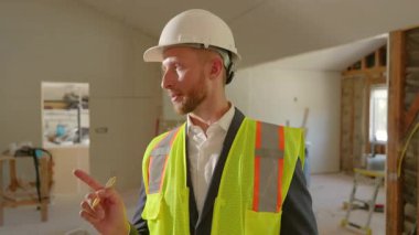 Güvenlik yeleği giyen kendini adamış bir şantiye müdürü önemli konut tadilatı belgelerini gözden geçirir ve başarılı bir infaz için her şeyin hazır olduğundan emin olur.