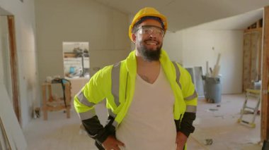 Şatafatlı ceketli ve kasketli neşeli bir inşaat işçisi, bir şantiyede güven içinde duruyor. Güvenliğe, mükemmeliyetçiliğe ve profesyonelliğe olan bağlılıklarını gösteriyor.