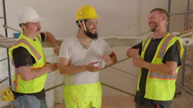 Çeşitli müteahhitlerden oluşan bir ekip, ev yenileme çalışmalarının yoğun olduğu bir inşaat sahasında, aletlerle donatılmış ve beklenti ve yaratıcılık dolu bir tebessümle ilgili planları aktif olarak tartışıyor.