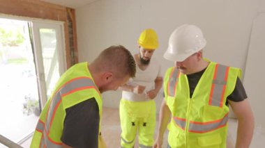 Parlak güvenlik yelekleri ve kask giyen kendini adamış inşaat ekibi, yenilenmiş iç mekanda yaralı işçi durumuyla meşgul, ilk yardım gerekli.