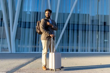 Bir adam telaşlı bir havaalanında duruyor, bavulunu sıkıca kavrıyor, heyecanlı bir şekilde beklenen bir yolculuğa hazır, hepsi de gezgin şehvetini körükleyen nefes kesen mimari bir zemin tarafından çerçevelenmiş.
