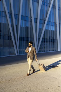 Parlak gündüz saatlerinde şık bir evrak çantası taşıyan, modern mimari ile canlı bir şehir manzarası boyunca, özel dikim bir takım elbise giymiş parlak bir profesyonel, emin adımlarla ilerler.