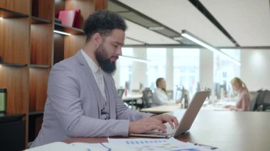 Kendini işine adamış ve çalışkan bir iş adamı tamamen bilgisayarına odaklanırken, aynı zamanda çağdaş bir ofis ortamında, dinamik bir çalışma alanı içinde olağanüstü üretkenlik sergiliyor.