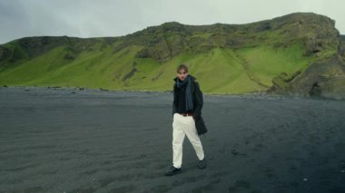 Genç adam, Reynisfjara 'nın büyüleyici ve büyüleyici siyah kumsal sahillerinde, İzlanda' nın eşsiz ve nefes kesici manzarasını ve farklı coğrafyasını sergiliyor.